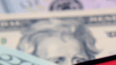 Imagen de un celular que está sobre unos billetes de color verde y en su pantalla de ve el logotipo de la empresa Airbnb en blanco con rojo.