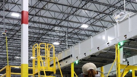 Imagen de una trabajadora de Amazon que tira de una plataforma en la que están colocados decenas de paquetes y cajas de cartón.