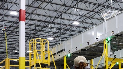 Imagen de una trabajadora de Amazon que tira de una plataforma en la que están colocados decenas de paquetes y cajas de cartón.