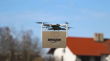 Imagen de un dron que transporta una caja de cartón con el logotipo de Amazon.