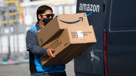 Imagen de un repartidor de Amazon que carga dos cajas de cartón, a un costado de una camioneta.