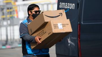 Imagen de un repartidor de Amazon que carga dos cajas de cartón, a un costado de una camioneta.
