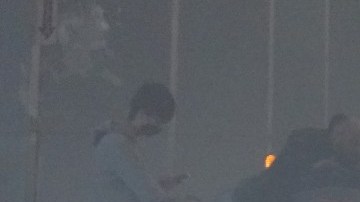 Imagen de una persona que está sentada en el piso de un aeropuerto en medio de dos maletas.