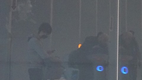 Imagen de una persona que está sentada en el piso de un aeropuerto en medio de dos maletas.