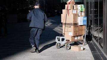 Imagen de una persona que está repartiendo paquetes, junto a una plataforma para llevarlos.
