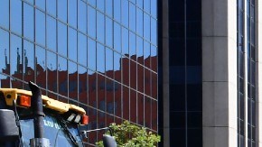 Imagen de una persona que realiza trabajos en la vía pública, junto a una máquina excavadora.