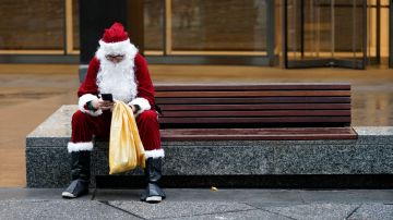 Imagen de una persona personificada como Santa Claus sentada en una banca, con una bolsa en la mano.