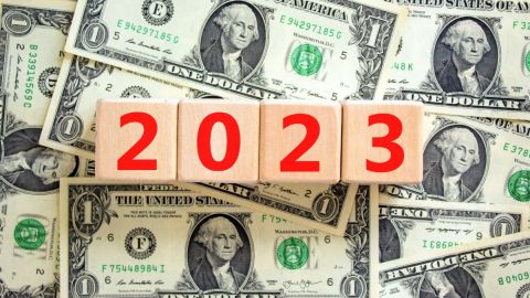 Imagen de muchos billetes y de cuatro cubos de madera que tienen los números del año 2023.