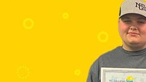 Imagen de dos personas que sostienen un cheque de gran tamaño con ambas manos, parados frente a un fondo de color amarillo.