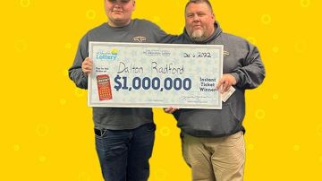Imagen de dos personas que sostienen un cheque de gran tamaño con ambas manos, parados frente a un fondo de color amarillo.