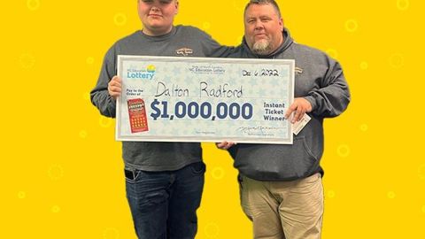 Imagen de dos personas que sostienen un cheque de gran tamaño con ambas manos, parados frente a un fondo de color amarillo.
