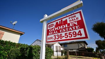 Imagen de un letrero de venta de vivienda en color rojo y blanco, puesto en el jardín de una casa.