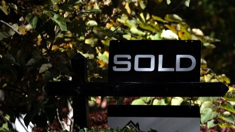 Imagen de varias personas que caminan a un costado de un letrero de venta de vivienda.