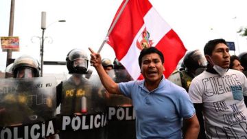 Un simpatizante del expresidente Pedro Castillo ondea una bandera nacional frente a la policía antidisturbios.