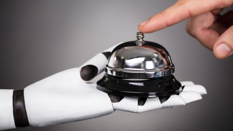 Imagen de una mano robotizada que sostiene una campana, mientras el dedo de una persona presiona un botón.