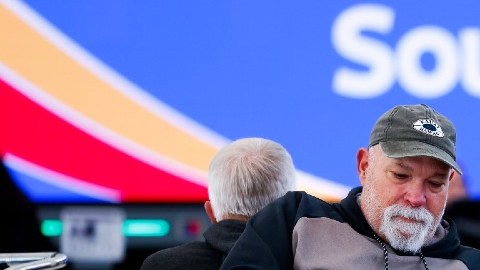 Imagen de dos personas que están sentadas en un aeropuerto, en medio de maletas de equipaje.
