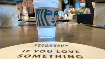 Imagen de un vaso de Starbucks que están colocado sobre una barra de entrega de madera y en la que se ve un letrero de promoción del programa Starbucks Rewards.