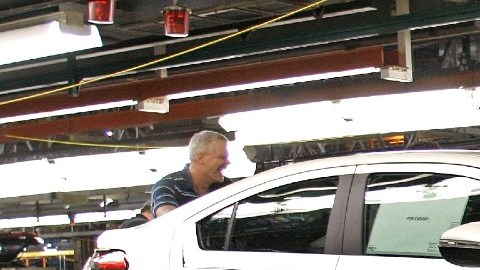 Imagen de dos trabajadores que mueven un vehículo en una línea de construcción de General Motors.