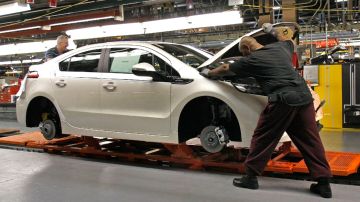 Imagen de dos trabajadores que mueven un vehículo en una línea de construcción de General Motors.