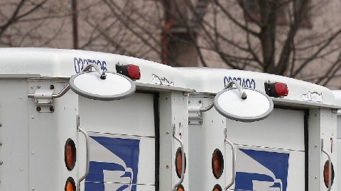 Imagen de una flota de camiones de color blanco con detalles en azul y rojo del Servicio Postal de Estados Unidos.