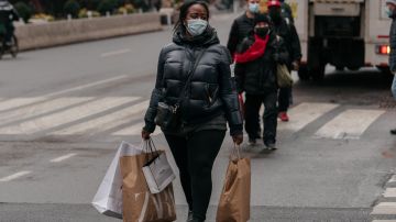 Imagen de una persona que carga bolsas de compras mientras cruza una calle.