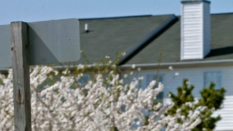 Imagen de un jardín letreros de venta de vivienda, frente a una casa y una camioneta de color blanco.