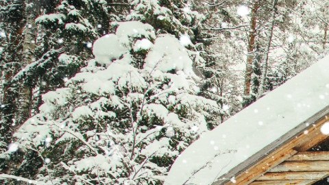 Imagen de una cabaña nevada y de un Santa Claus de pie frente a su puerta.