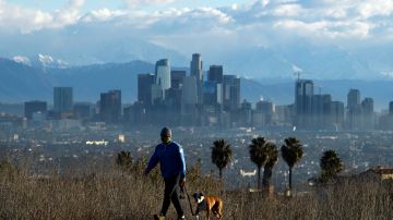 A person walks a dog as snow-topped mountains stand behind the Los Angeles downtown skyline after sunrise following heavy rains as seen from the Kenneth Hahn State Recreation Area on December 29, 2020 in Los Angeles, California. (Photo by Patrick T. FALLON / AFP) (Photo by PATRICK T. FALLON/AFP via Getty Images)