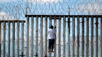 Un migrante mexicano deportado cuelga cruces de madera en la valla fronteriza en una vigilia por los migrantes fallecidos en julio de 2022.