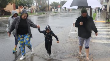 Angélica Barba, Lissette Martínez, Cassandra Williams y la pequeña Leilani cruzan una calle en medio del agua anegada.