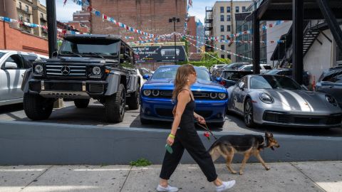 Imagen de una persona que camina frente a tres vehículos que están estacionados en un negocio de venta de autos usados.
