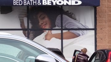 Imagen de una publicidad de la tienda Bed Bath & Beyond, en medio de un estacionamiento, en el que se ve a una persona subiendo a un automóvil.