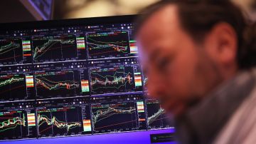 Imagen de una persona fuera de foco en el piso de remates de Wall Street, en el que se ven varias pantallas con indicadores.