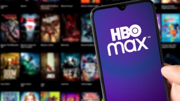 Imagen de una persona que muestra un celular en cuya pantalla se ve el logotipo de la aplicación HBO Max, en colores morado y blanco.