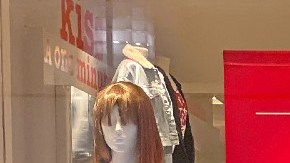 Imagen de una persona vestida con un suéter rojo que camina frente a un aparador de cristal en el que se ven letreros de descuentos.