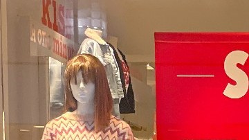 Imagen de una persona vestida con un suéter rojo que camina frente a un aparador de cristal en el que se ven letreros de descuentos.