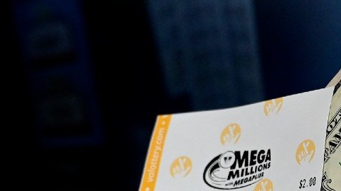 Imagen de una persona que muestra un boleto del sorteo Mega Millions y de billetes de un dólar.