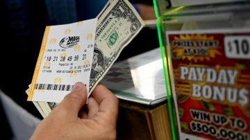 Imagen de una persona que muestra un boleto del sorteo Mega Millions y de billetes de un dólar.