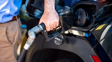 Una persona que sostiene un despachador de gasolina para cargar combustible en su auto.