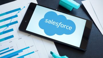 Imagen de un celular en cuya pantalla se ven un logotipo de la empresa Salesforce, sobre unos papeles y un marcador de color azul.
