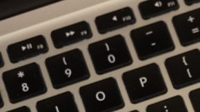 Imagen de la pantalla de un teléfono celular con el logotipo de la empresa Shopify, colocado sobre el teclado de una computadora.