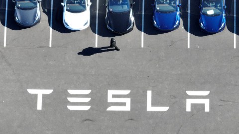Imagen de varios vehículos de Tesla estacionados y de unas letras de color blanco con la frase Tesla.