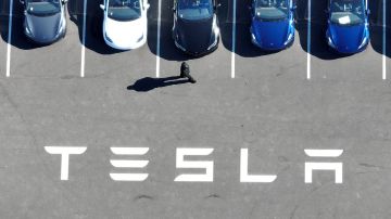 Imagen de varios vehículos de Tesla estacionados y de unas letras de color blanco con la frase Tesla.