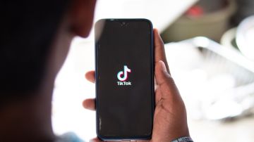 Imagen de una persona que sostiene un teléfono con la mano y en cuya pantalla se ve un logotipo de la red social TikTok.