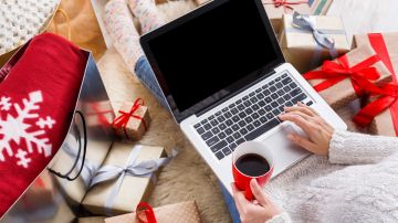 Imagen de una persona que sostiene una computadora y que está rodeada de regalos de Navidad.