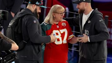 Donna Kelce, con un jersey de Eagles y Chiefs, les entrega galletas a sus hijos Jason (izq.) y Travis.