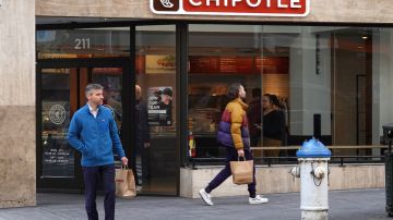 Imagen de un restaurante de la cadena Chipotle y afuera una persona con una chamarra azul que sostiene una bolsa.
