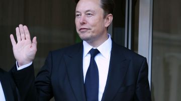 Imagen de Elon Musk con un traje de color negro que levanta el brazo para saludar.