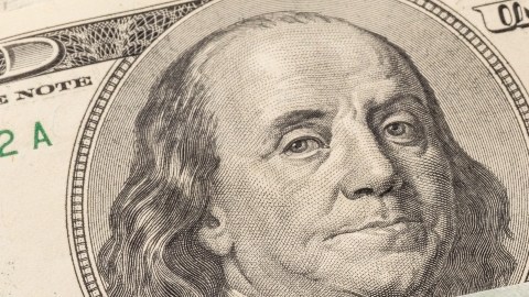 Imagen de un cheque de reembolso de impuestos y de varios billetes de $100 dólares.