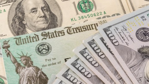 Imagen de un cheque de reembolso de impuestos y de varios billetes de $100 dólares.